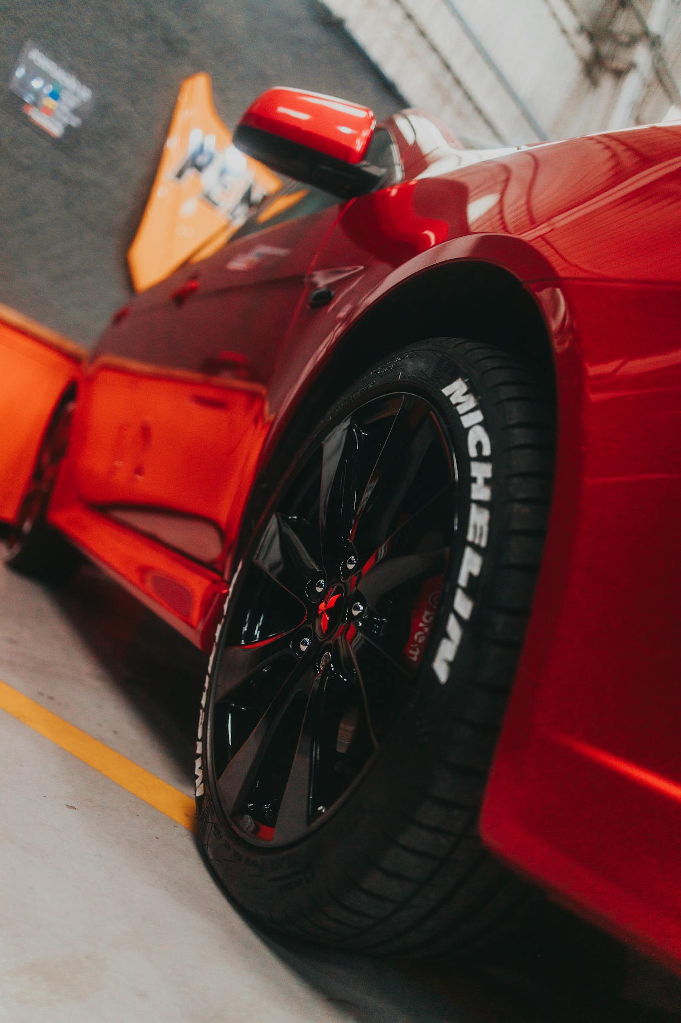 Close-up of a sleek red sports car showcasing a Michelin tire in a garage setting.